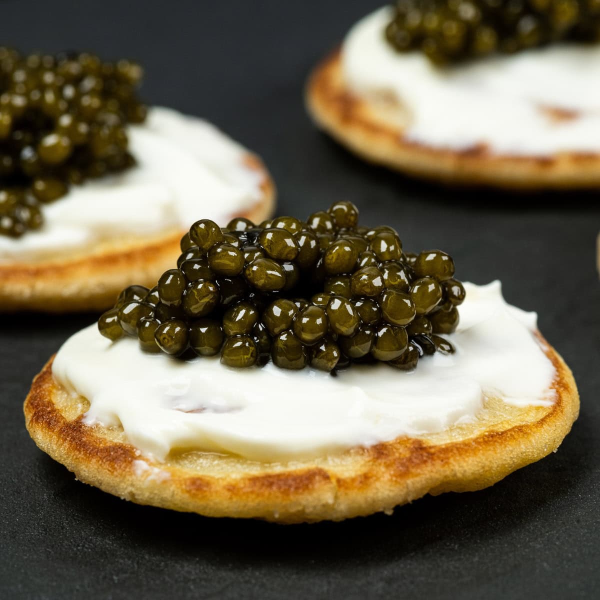 A close-up image of blini topped with luxury caviar, served on a dark surface.