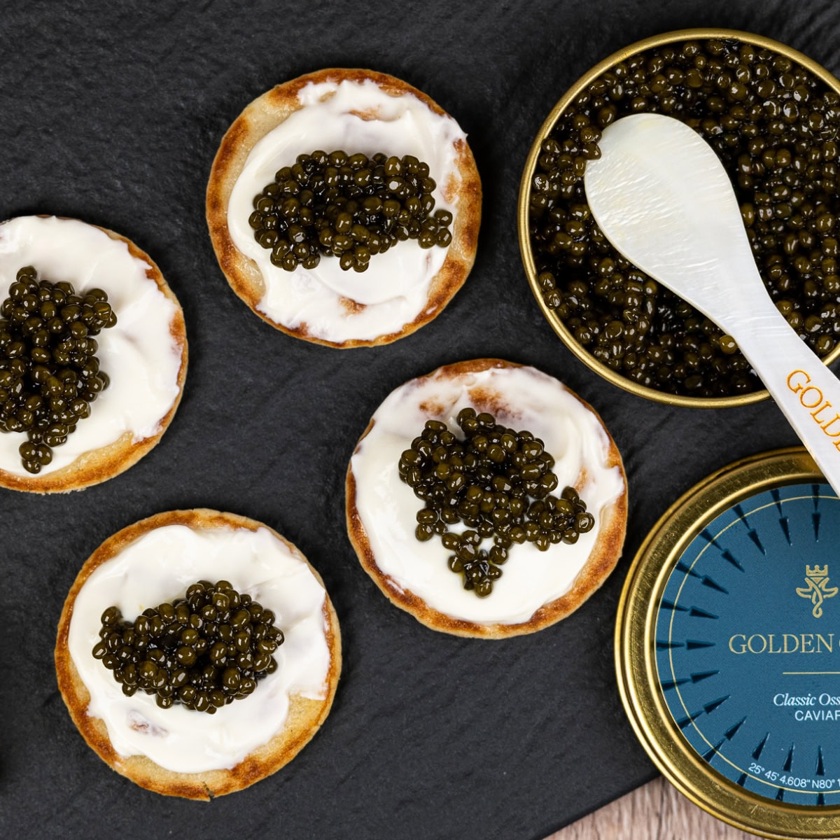 Dollop of cream with caviar on a cracker next to a caviar tin with a caviar spoon.