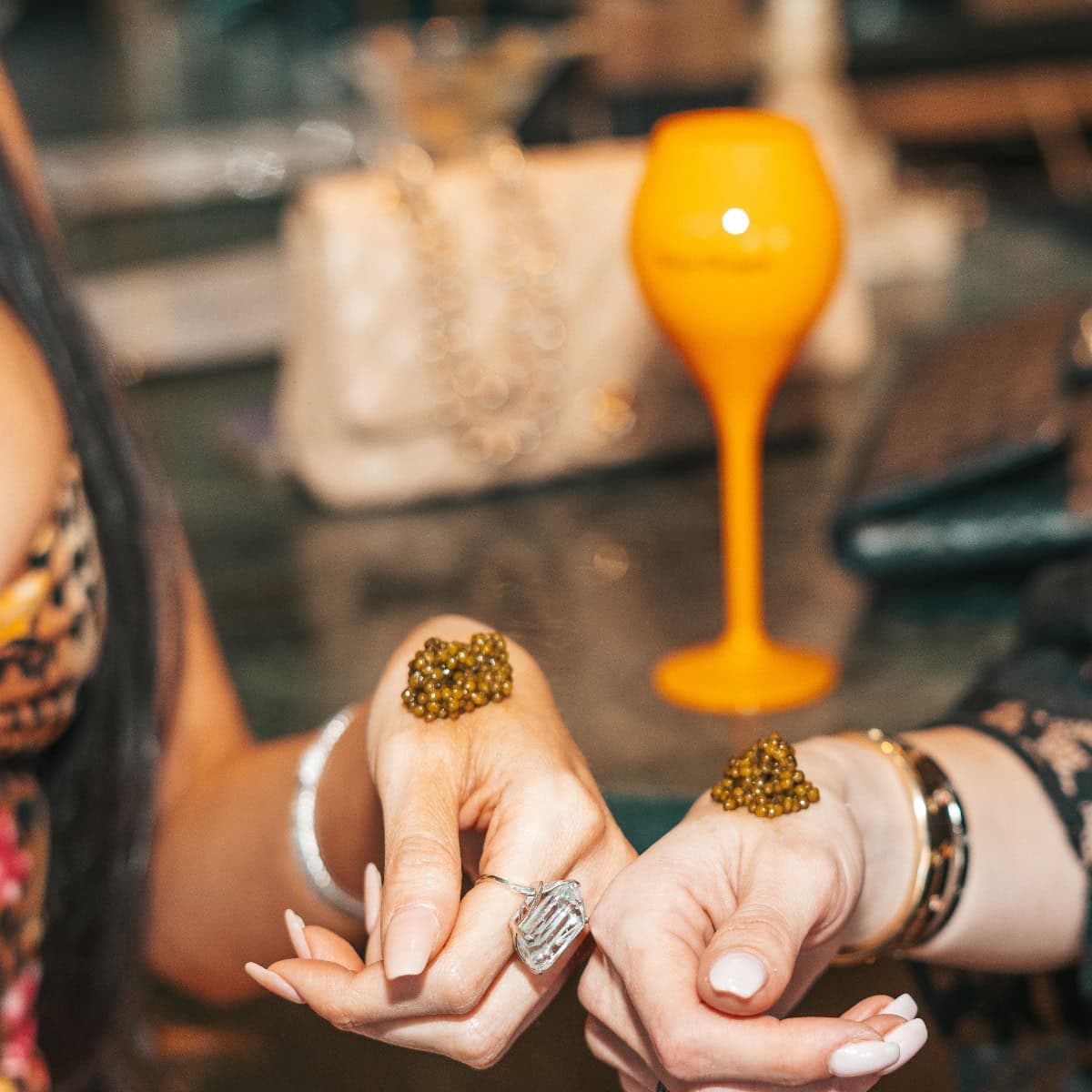Close-up of hands with rings and bracelets on a table with an orange object in the background.