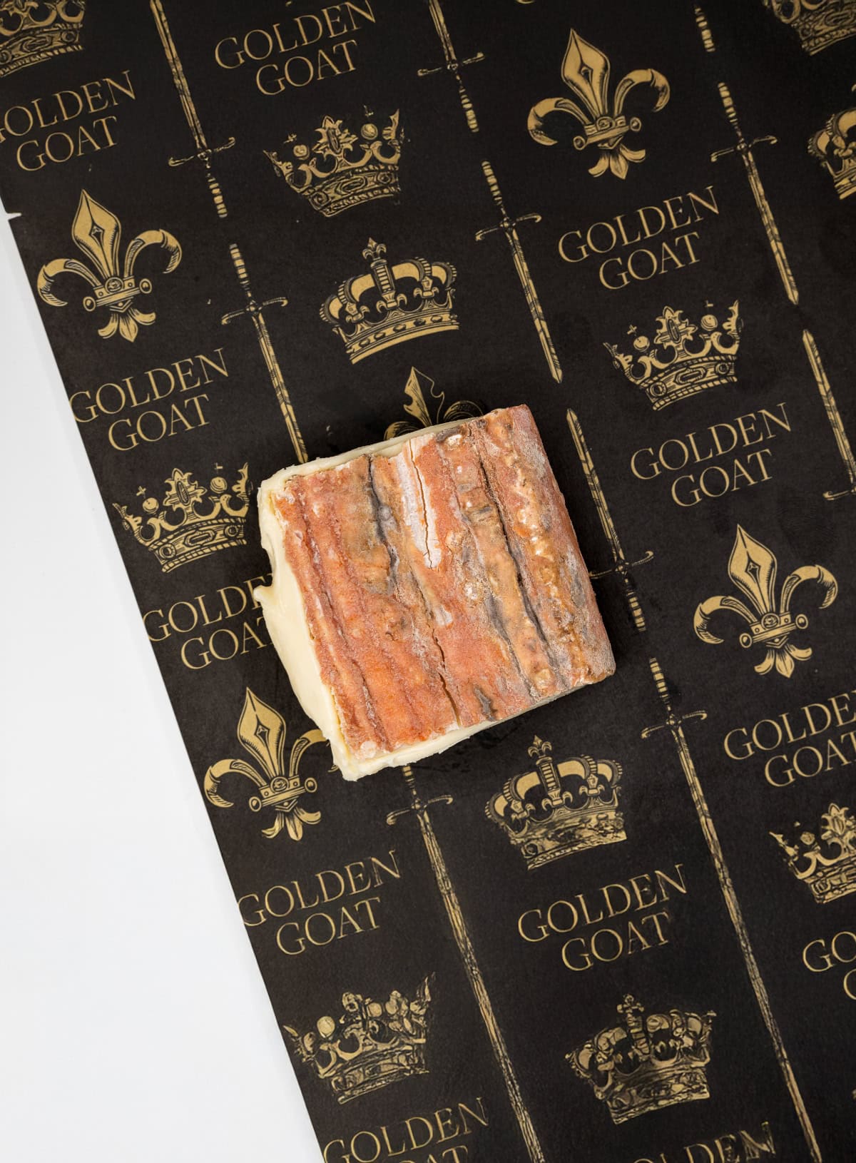 A block of Taleggio cheese with a rind on, placed on a paper packaging with 'GOLDEN GOAT' branding and crown motifs.