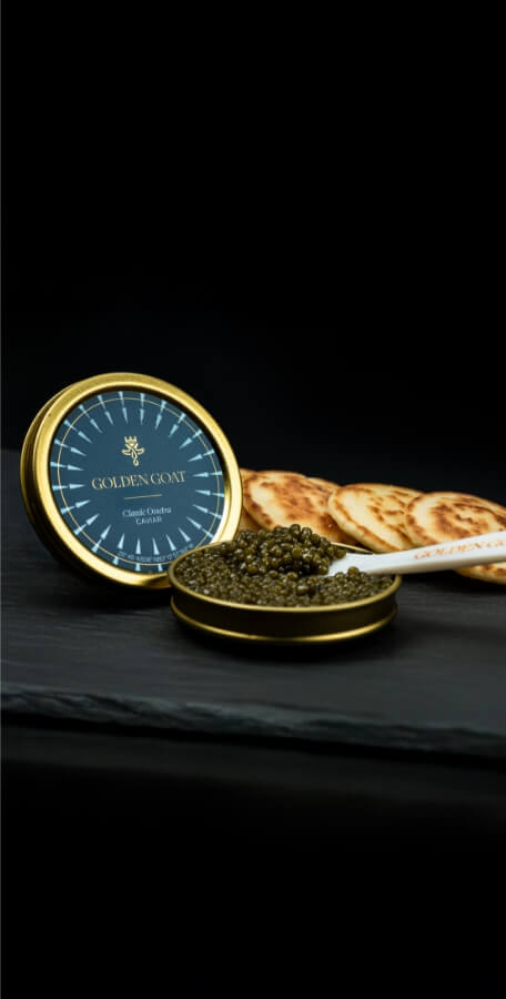 Caviar with a Golden Goat container with biscuits on a dark surface