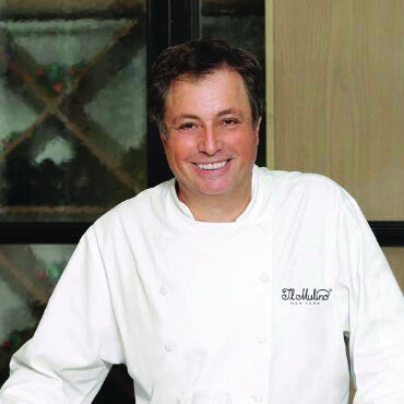 Person wearing a white chef's coat with a logo in an indoor setting