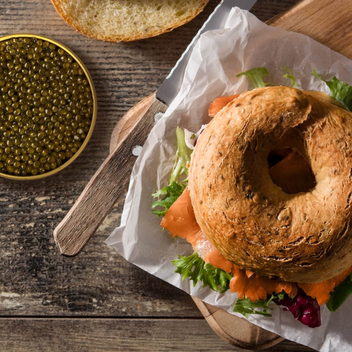 Bagel sandwich with salmon and vegetables on a wooden table with a tin of caviar.