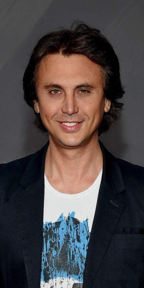 Man wearing a dark blazer over a white shirt with blue design on a gray background