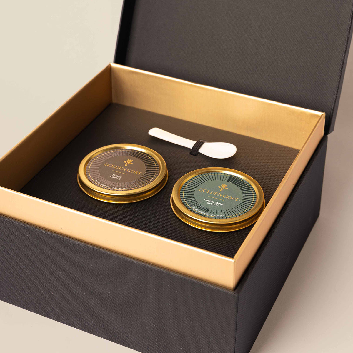 Two jars of caviar in a luxurious golden goat caviar gift box with a signature caviar key and pearl spoon.