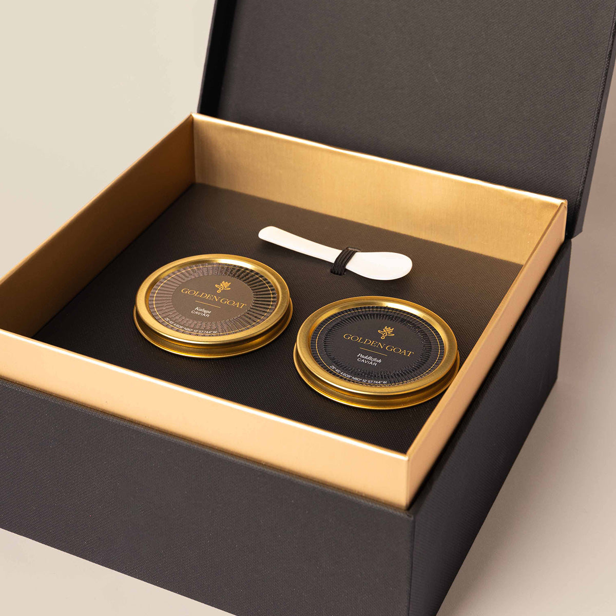Two tin containers of caviar in a luxurious golden goat gift box with a signature caviar key and pearl spoon.