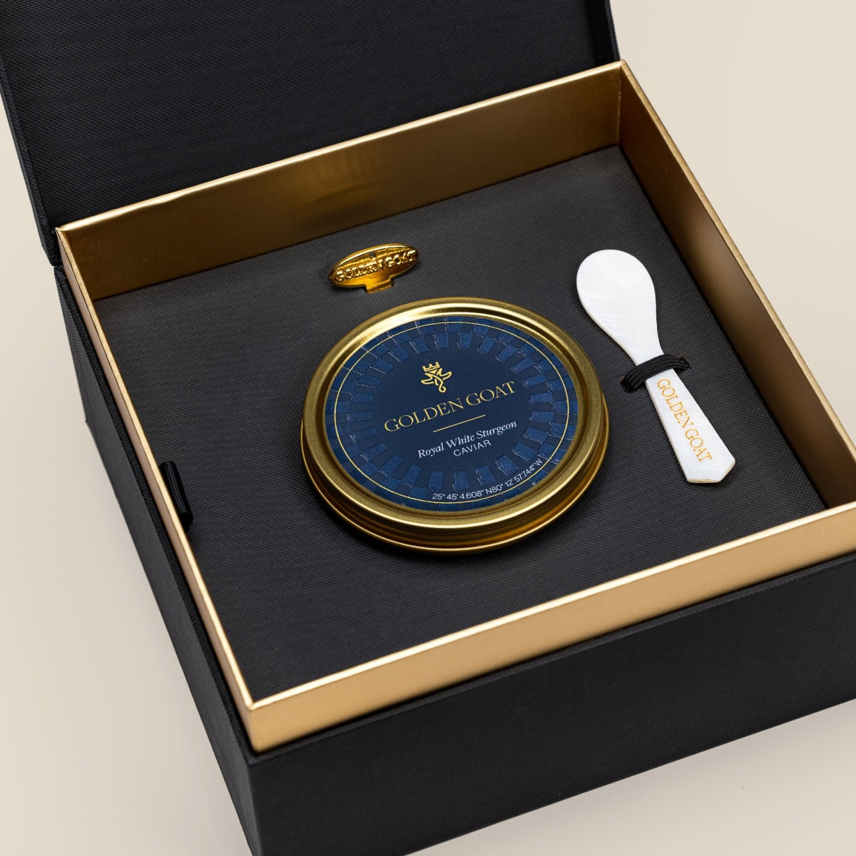 Caviar tin in a gift box with a caviar spoon and tin opener on a beige background.