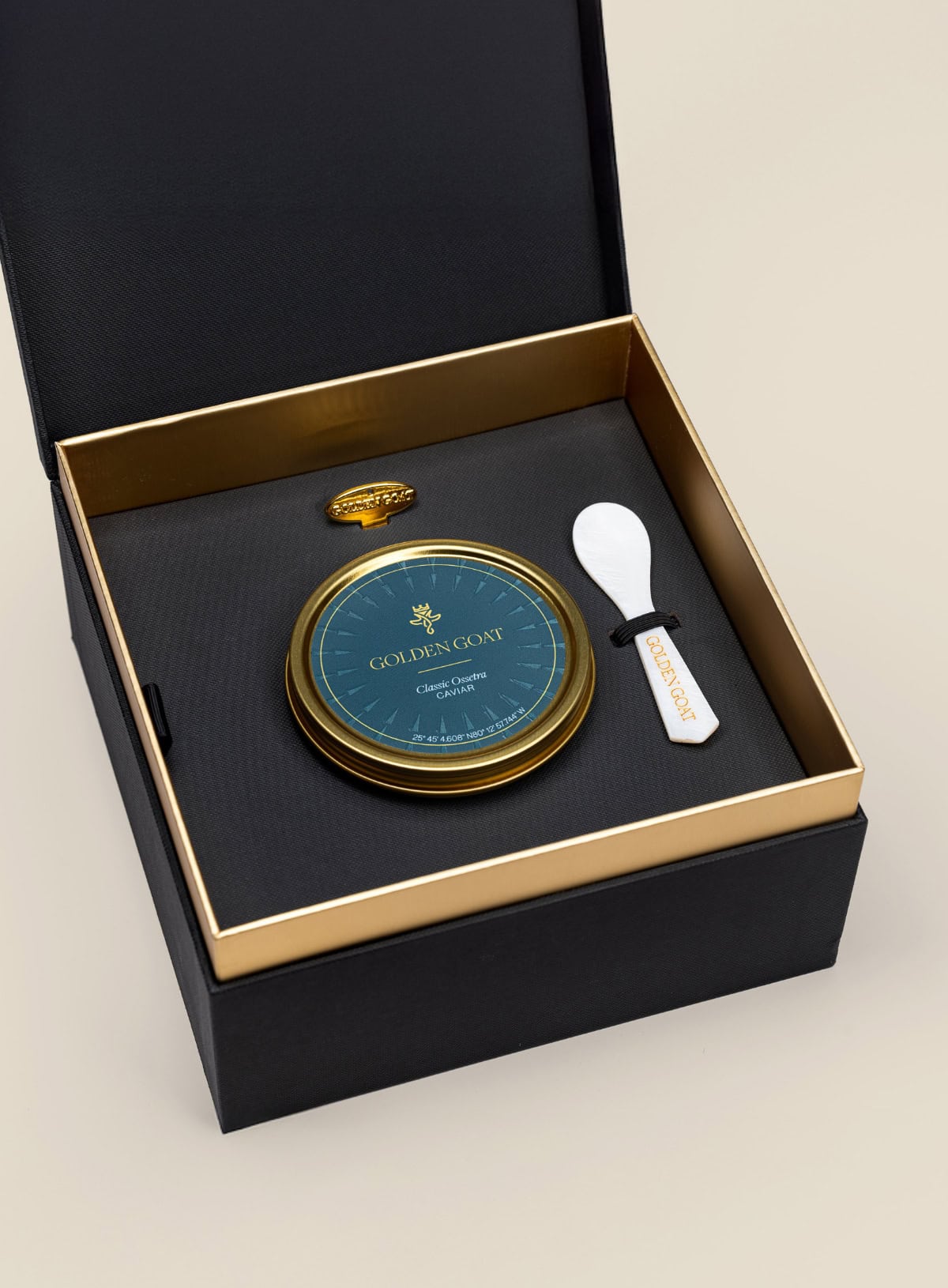 Golden goat caviar tin along in a caviar spoon and tin opener in a gift box on a beige background.