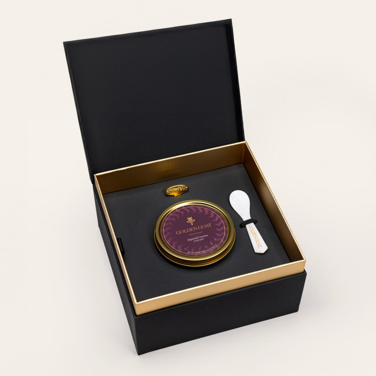 Black and gold box containing a gold caviar tin, caviar key, and pearl spoon on a white background.