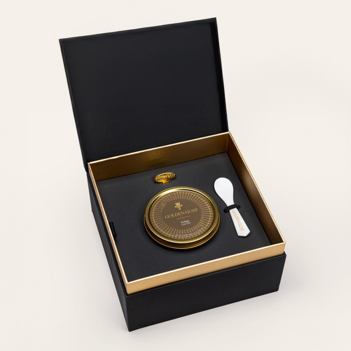 Black and gold box containing a gold caviar tin, caviar key, and pearl spoon on a white background.