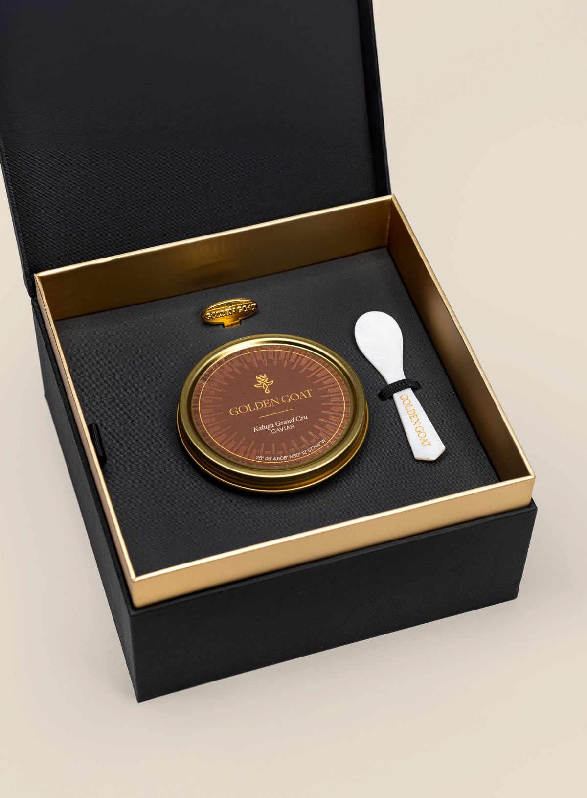 Caviar tin in a gift box with a caviar spoon and tin opener on a beige background.
