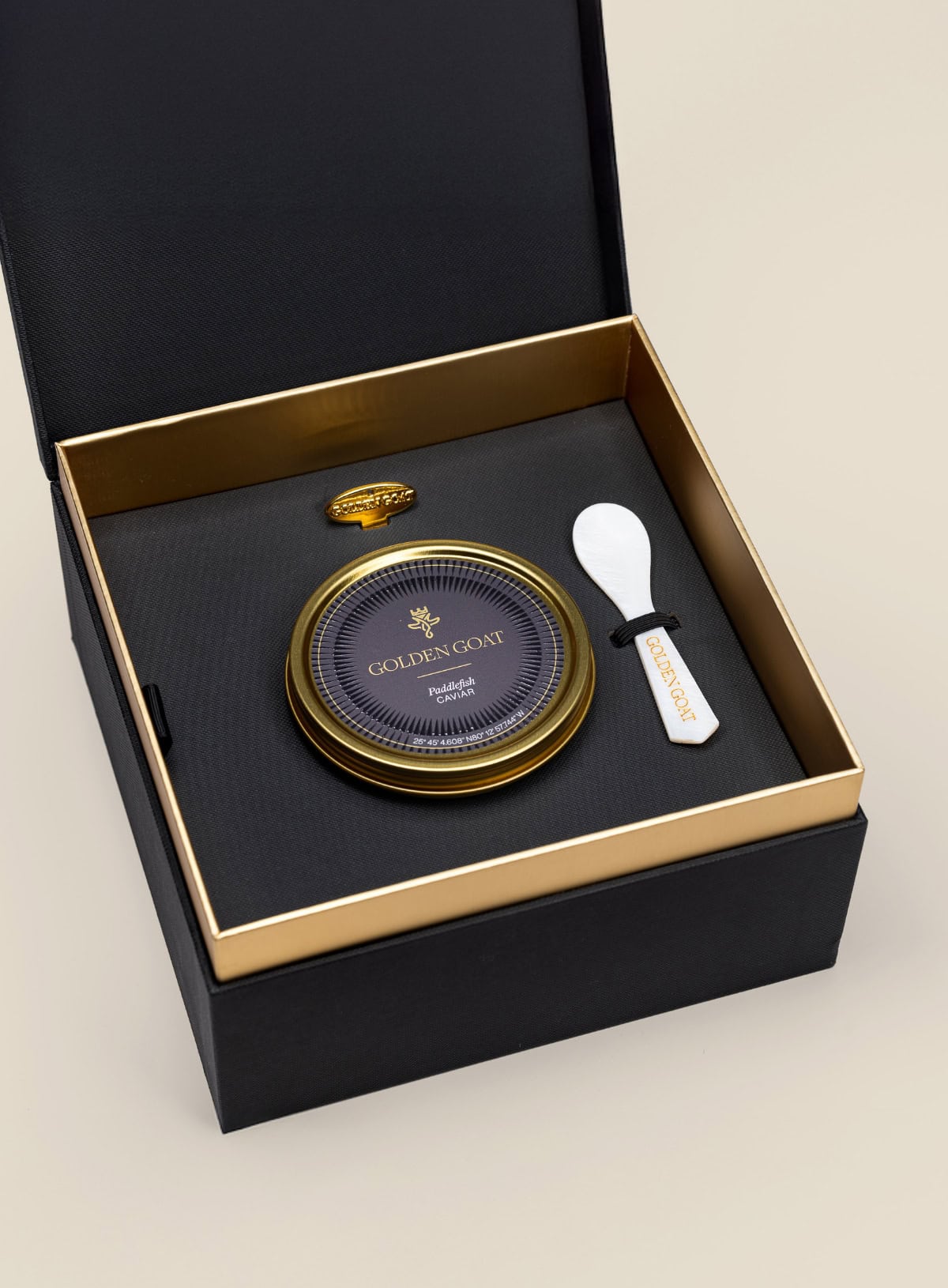 Caviar tin in a gift box with a caviar spoon and tin opener on a beige background.