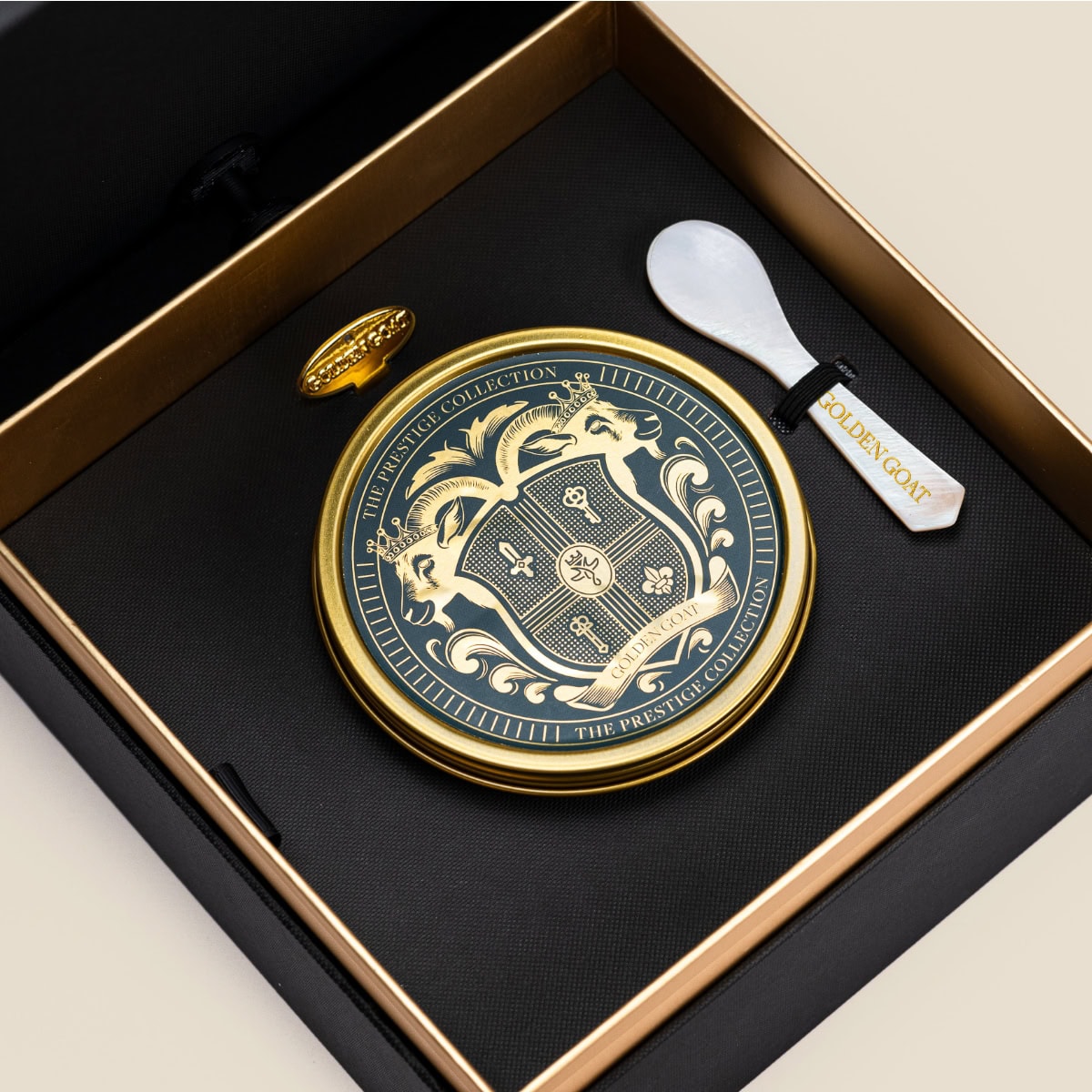 Tin of caviar in a box along with a caviar spoon and tin opener on a beige background.