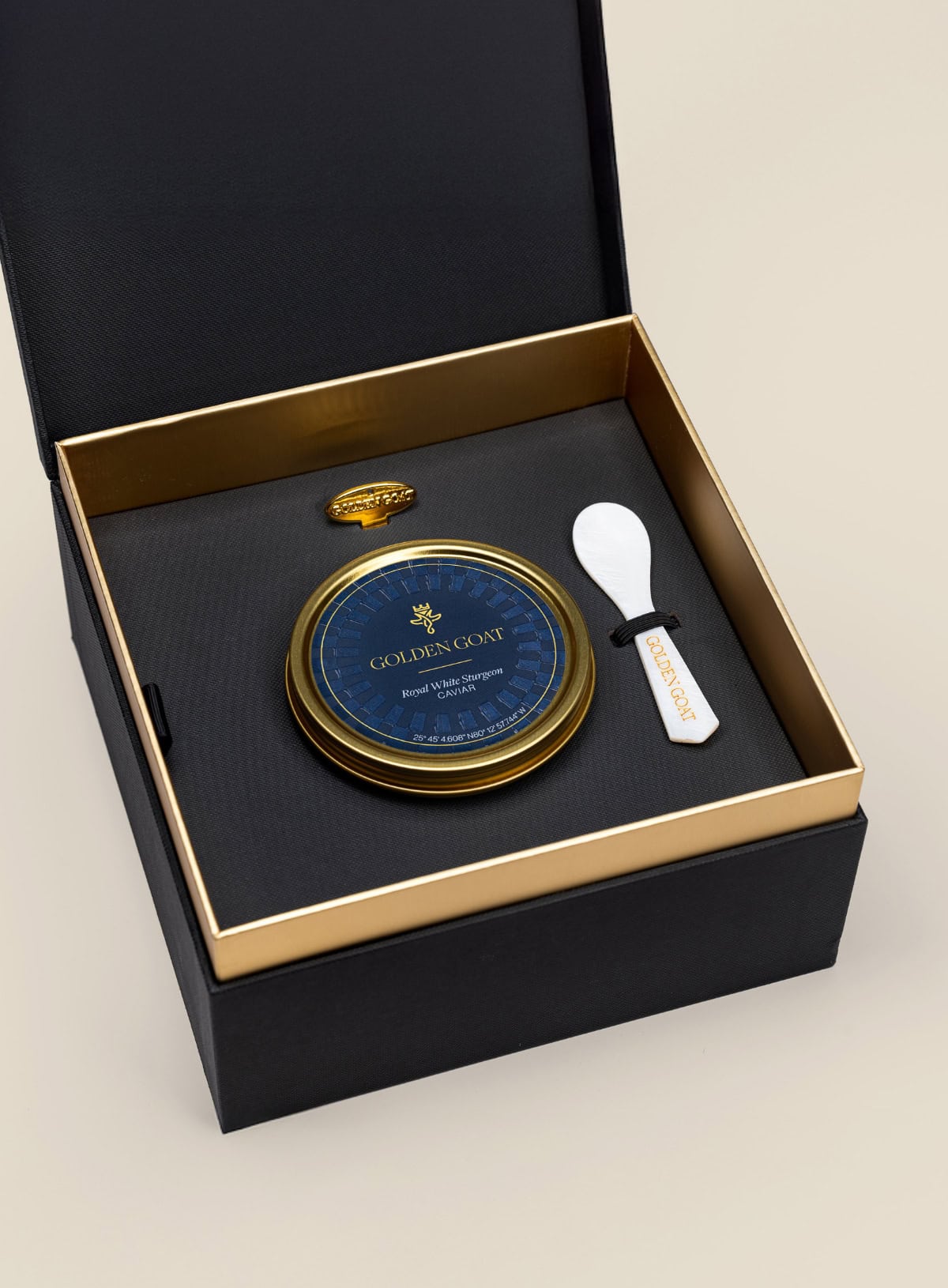 Caviar tin in a gift box with a caviar spoon and tin opener on a beige background.
