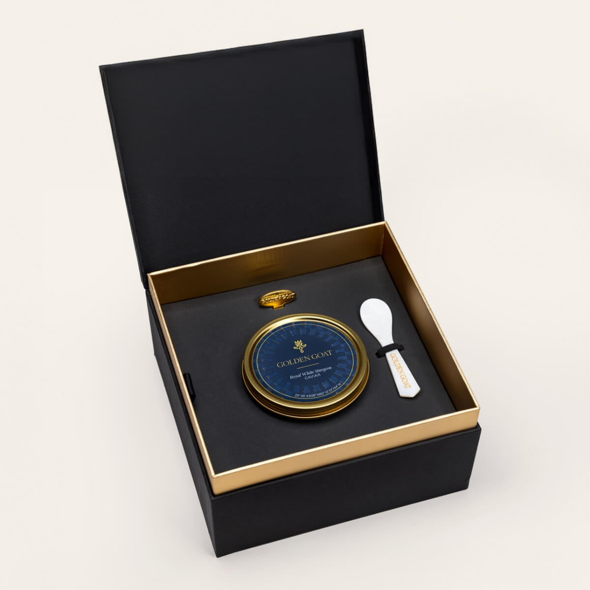 Black and gold box containing a gold caviar tin, caviar key, and pearl spoon on a white background.
