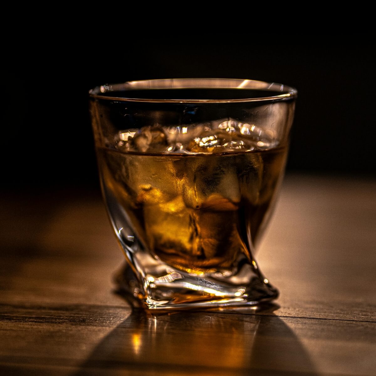 Glass of whiskey with ice cubes on a wooden surface