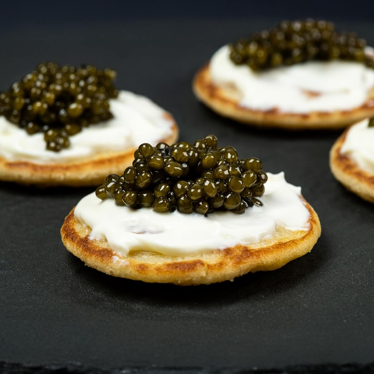 Blinis topped with cream and caviar on a dark surface