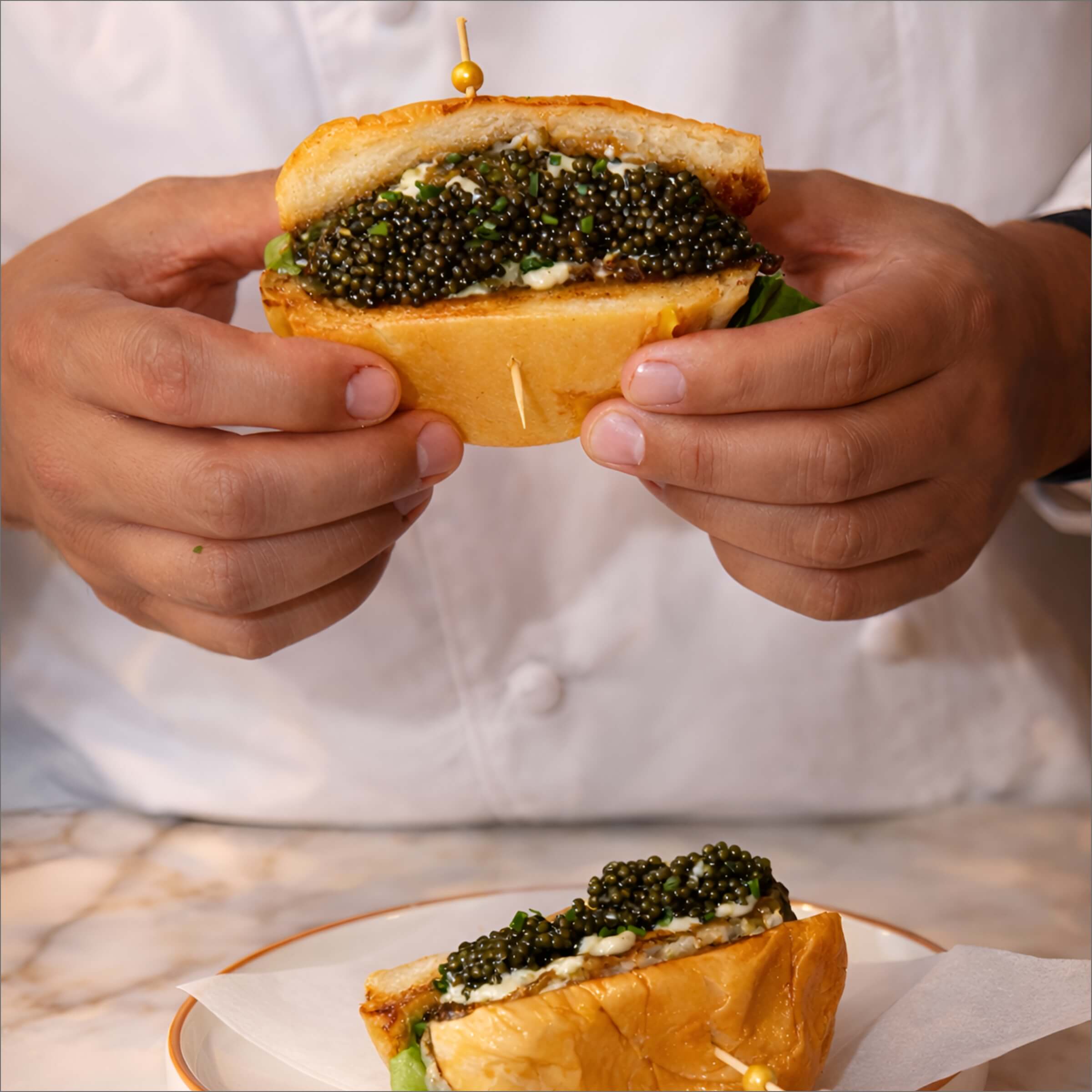 Chef holding a Burger topped with caviar.