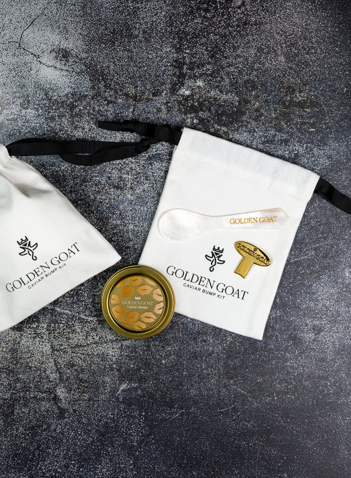An image featuring a white linen pouch with the brand name 'GOLDEN GOAT' on it, alongside a gold-plated caviar key and a tin of caviar.