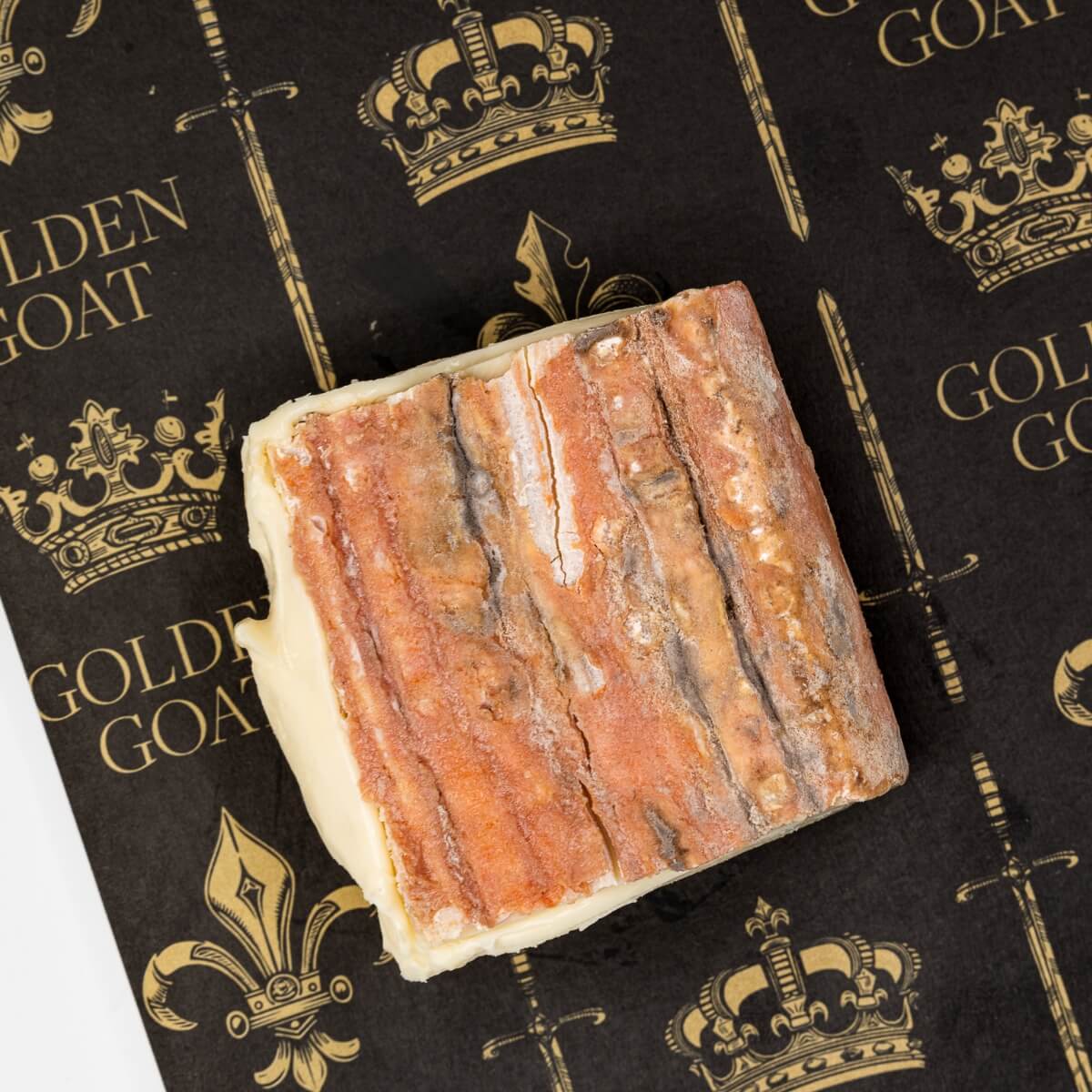 Block of Taleggio cheese on a black background with 'Golden Goat' branding.