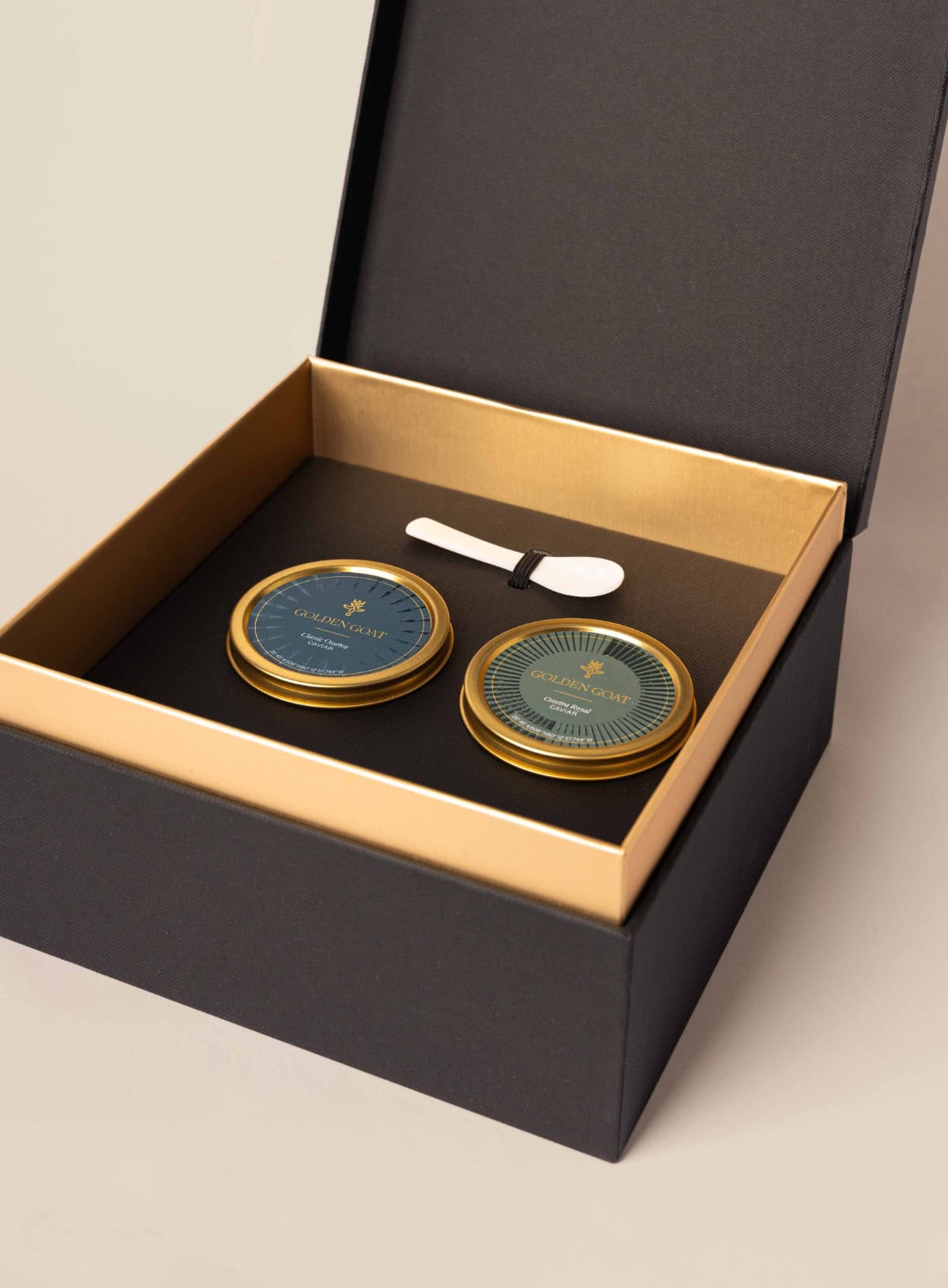 An open gift box displaying two jars of caviar brand Golden Goat, with a caviar key and spoon also present in the box.