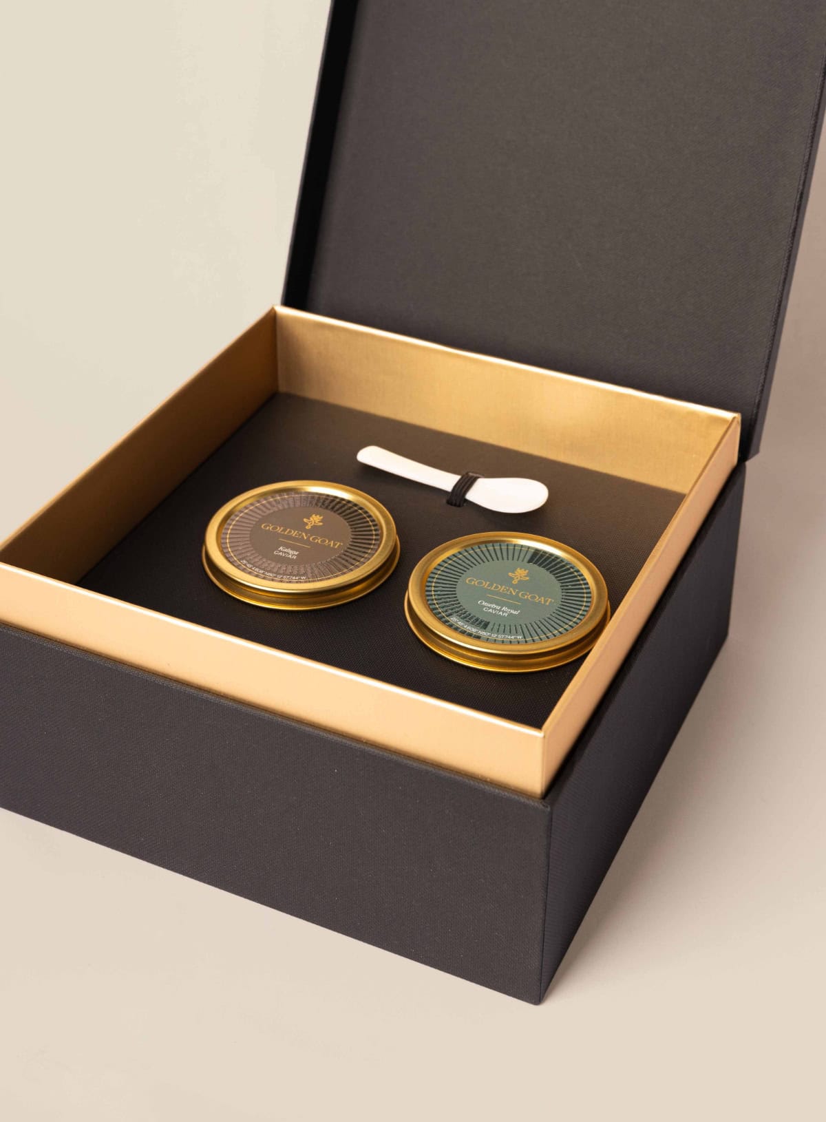 Two jars of caviar in a luxurious golden goat caviar gift box with a signature caviar key and pearl spoon.