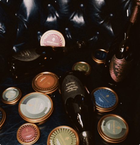 Collection of caviar various caviar tins with colorful designs along with champagne bottles on a dark leather couch.