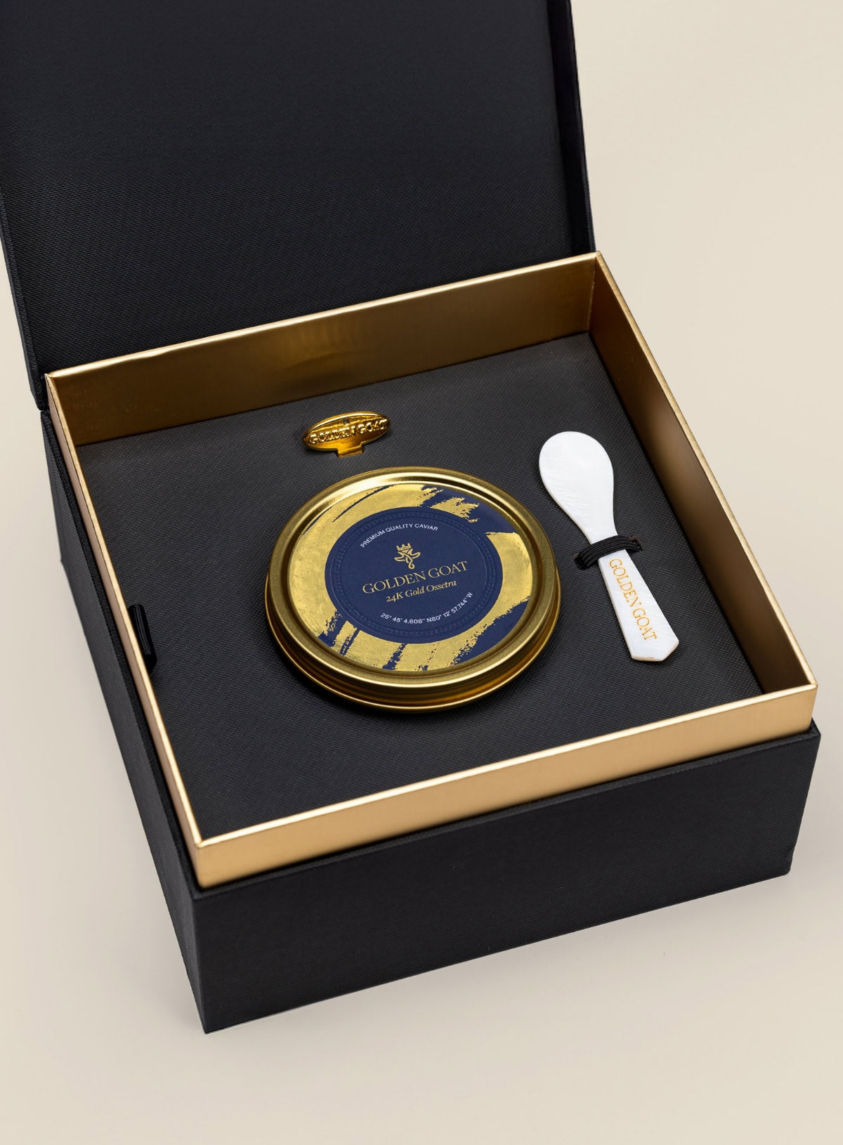 Gold and black caviar tin with a spoon in a black box on a beige background