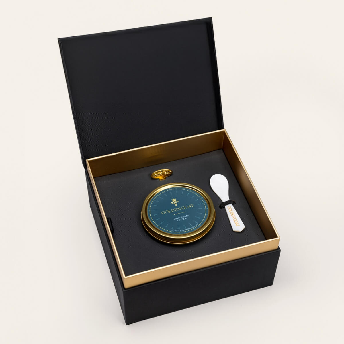 Black and gold box containing a gold caviar tin, caviar key, and pearl spoon on a white background.