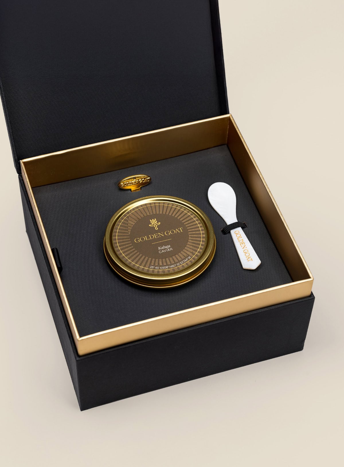 Caviar tin in a gift box with a caviar spoon and tin opener on a beige background.