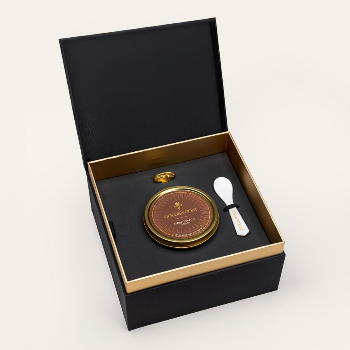Black and gold box containing a gold caviar tin, caviar key, and pearl spoon on a white background.