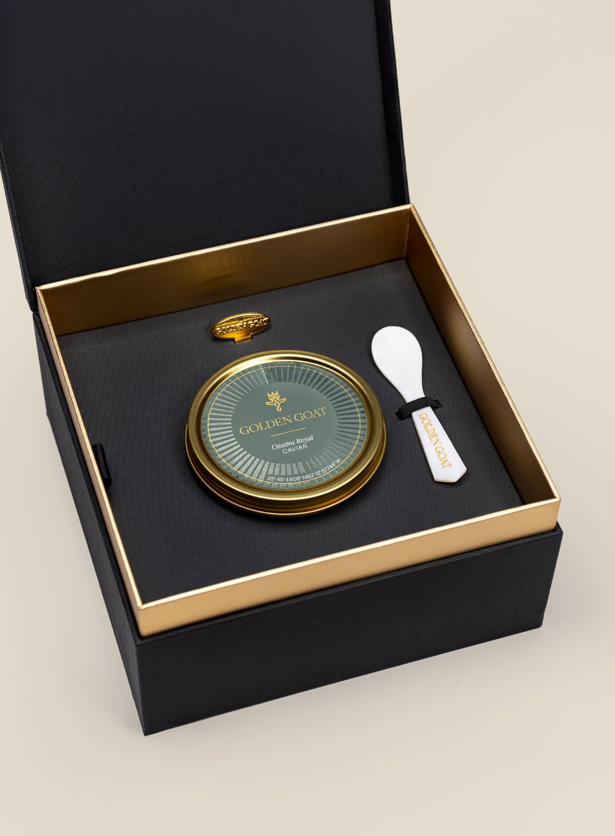 Black, gold, and green caviar tin with a spoon in a black box on a beige background
