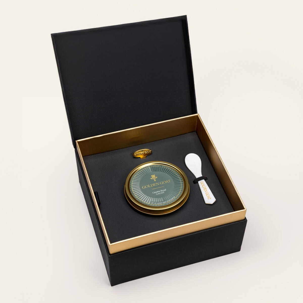 Black and gold box containing a gold caviar tin, caviar key, and pearl spoon on a white background.