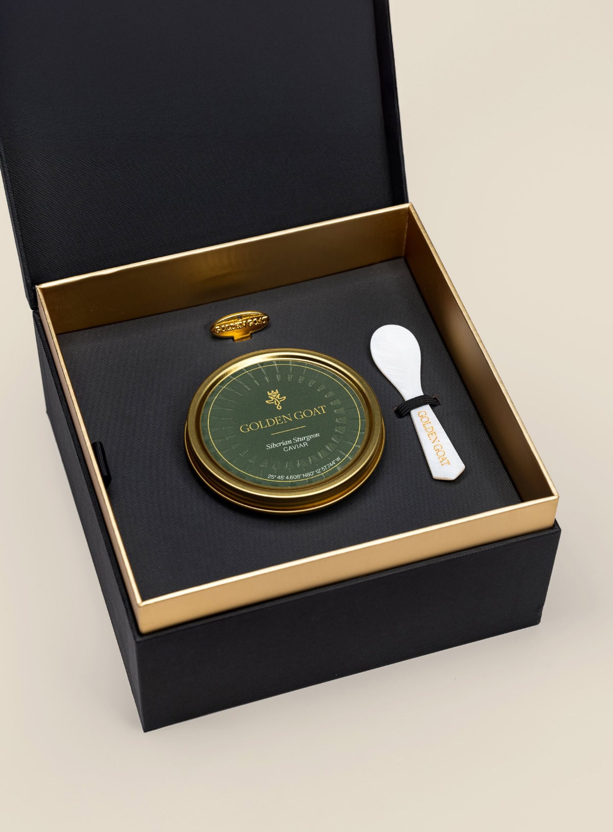 Caviar tin in a gift box with a caviar spoon and tin opener on a beige background.