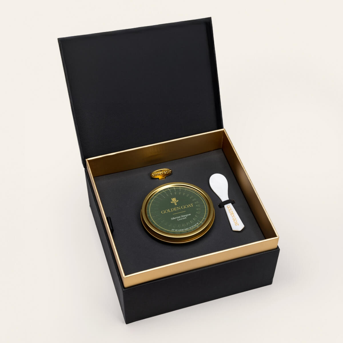 Black and gold box containing a gold caviar tin, caviar key, and pearl spoon on a white background.