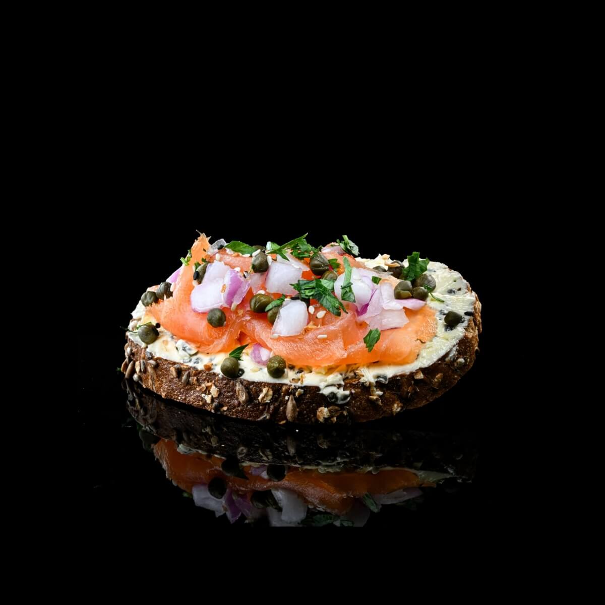 Smoked salmon and cream cheese on a piece of bread with caviar against a black background