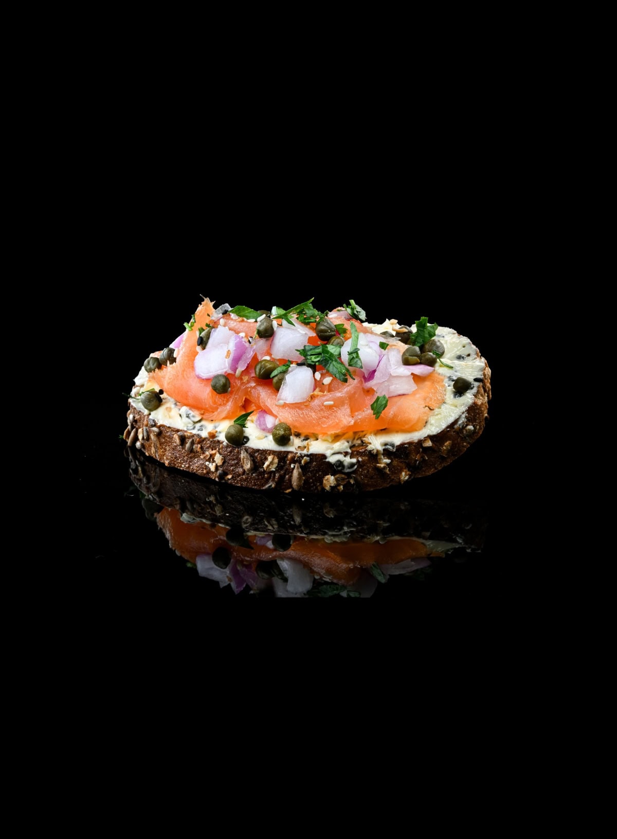 Smoked salmon and cream cheese on a piece of bread with capers and onions against a black background
